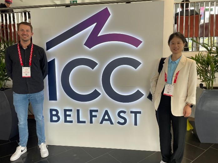 Zwei Personen stehen vor einem Brandingdisplay der „International Conference on Composite Materials“ in Belfast